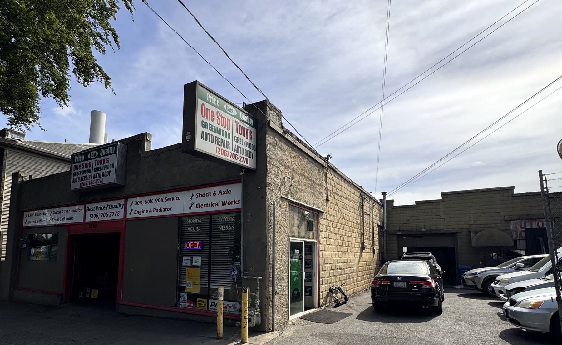 Wide view of Tony's Greenwood Auto Body lot, both signs, and neighboring shops