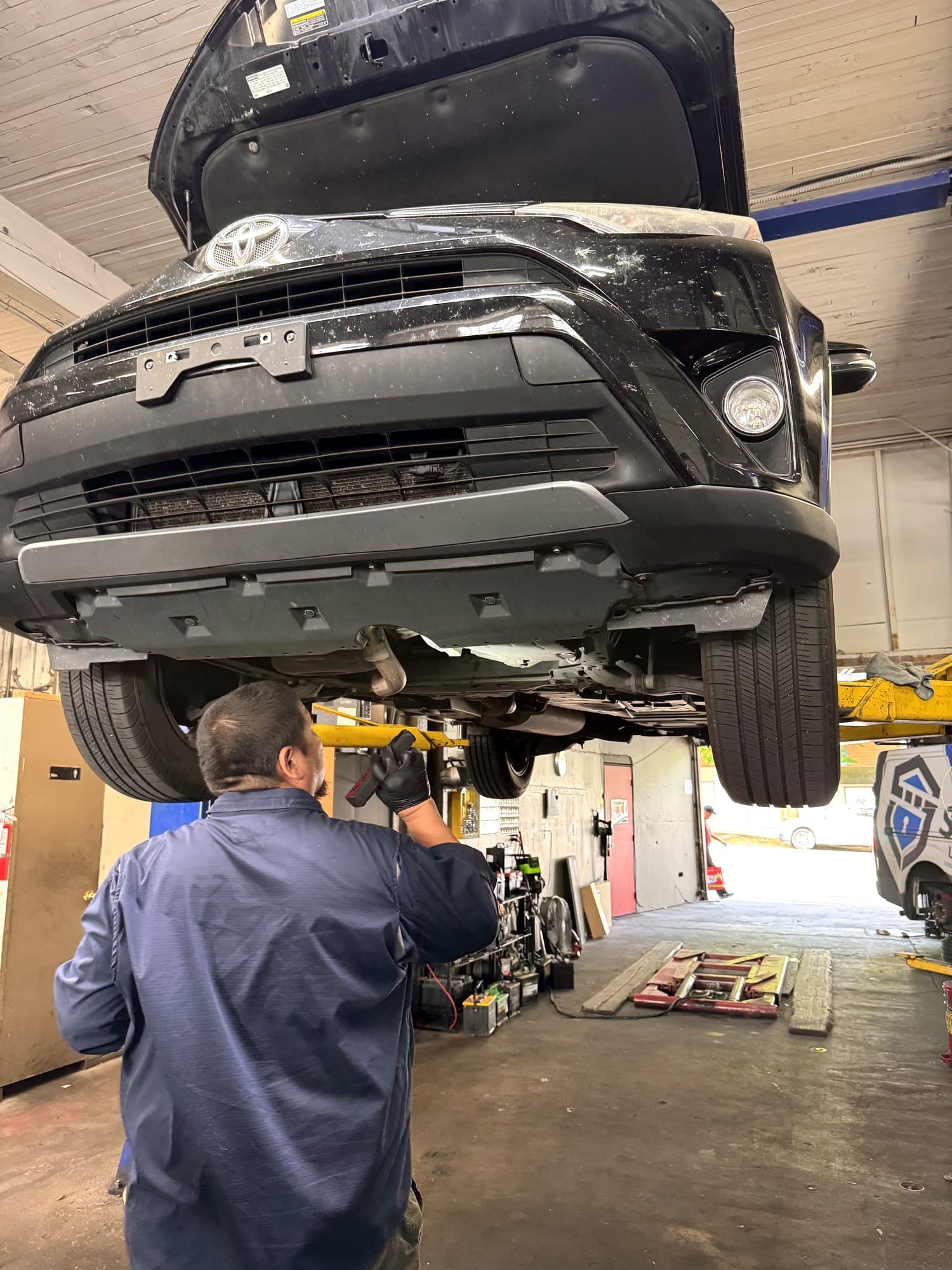 Technician with flashlight inspecting the underside of a raised RAV4